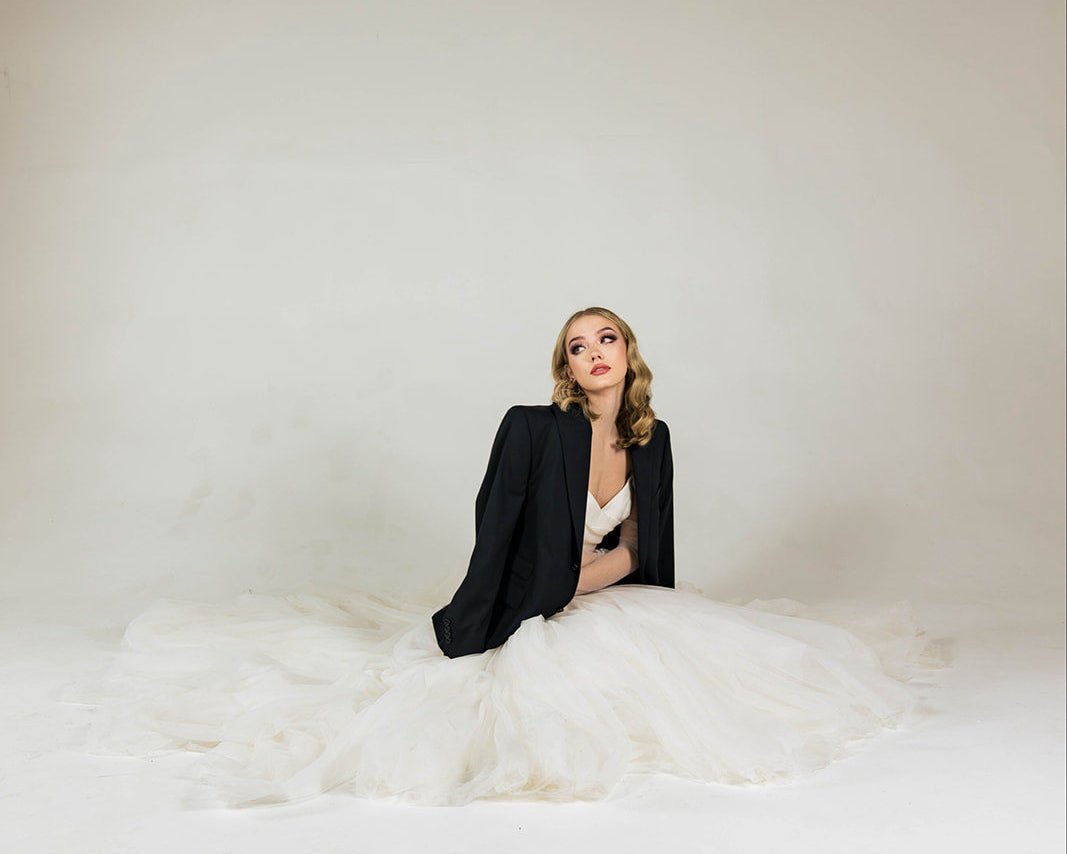 Editorial photo of a Duchess Boutique reception gown paired with a black tailored blazer, photographed in a minimalist studio setting.